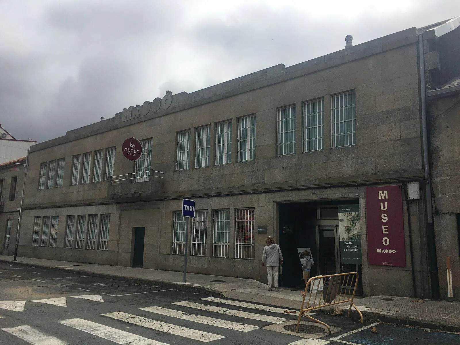 Fachada de piedra del Museo Massó con un cartel morado y la calle en primer plano
