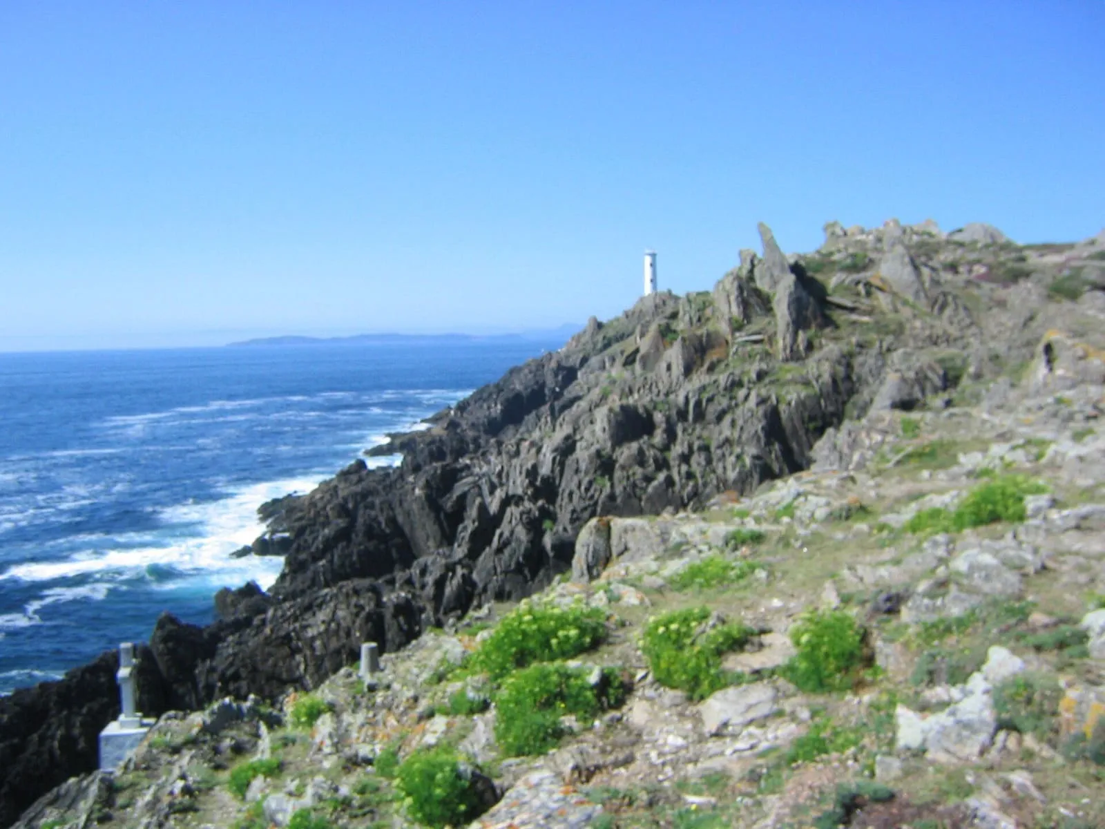 Costa rocosa de Cabo Home batida por el Atlántico, con el faro al fondo