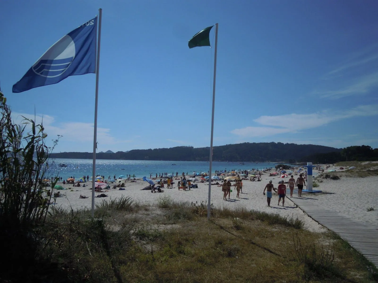 Playa de Nerga con las banderas azul y verde sobre la duna y bañistas al fondo