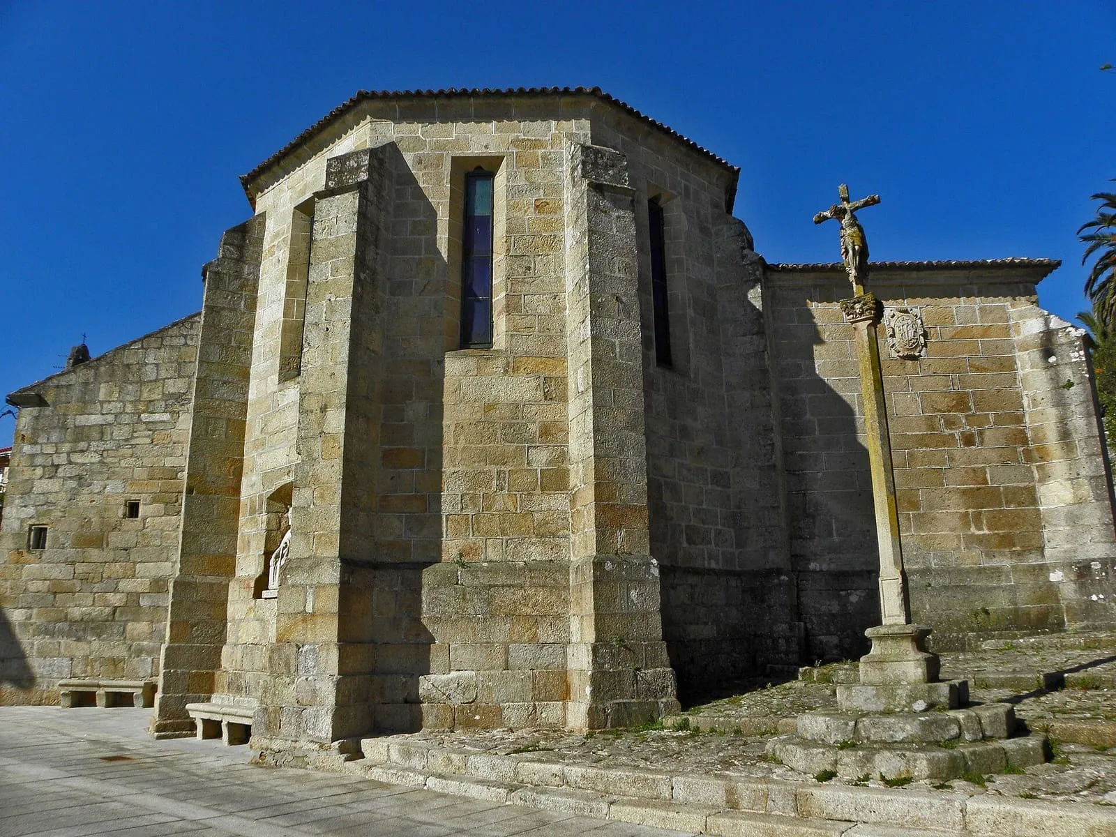 La iglesia de Santiago do Deán, de granito, con un cruceiro delante y el ábside gótico a la vista