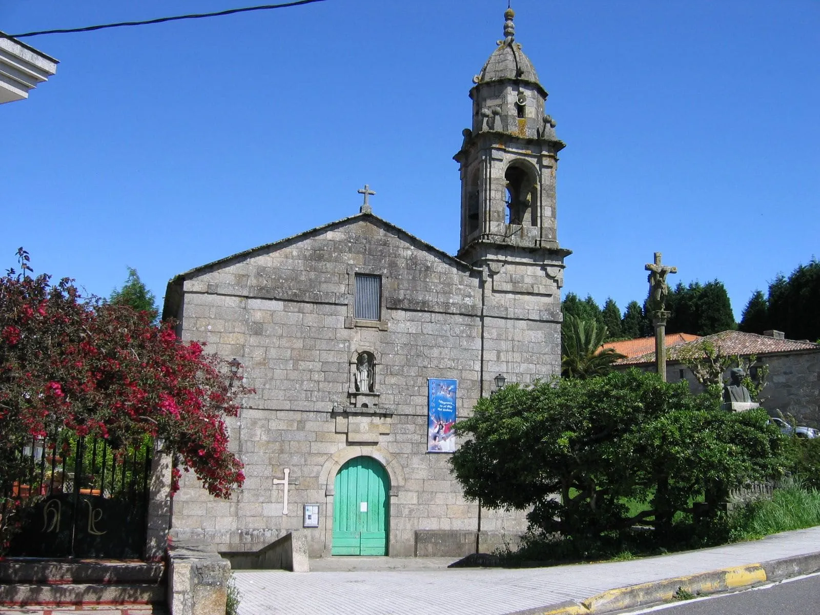 La iglesia de San Martiño do Grove, de piedra, con su campanario, un árbol y una calle delante