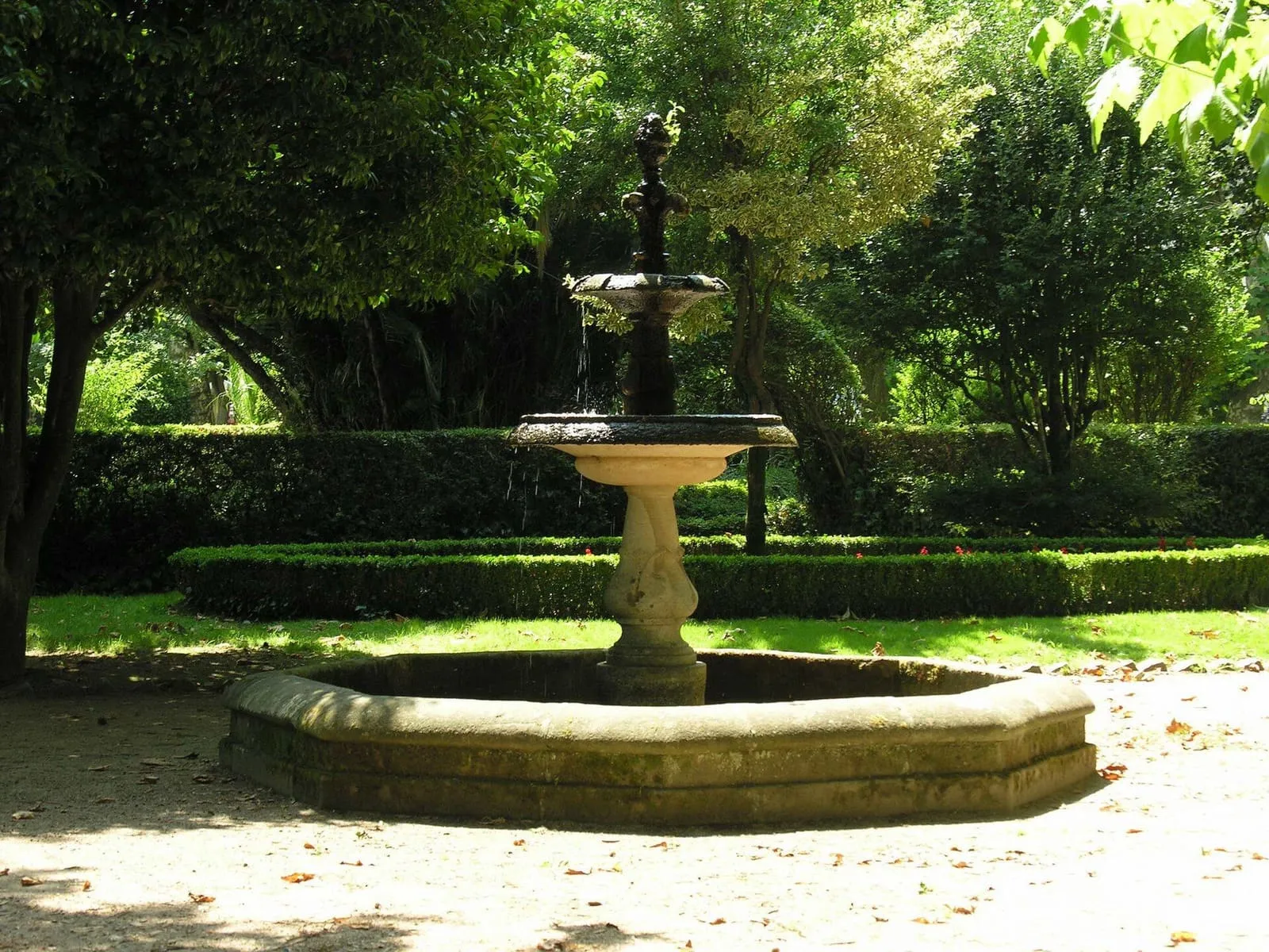 Fuente de piedra en un jardín de césped y arbolado en el jardín botánico de Padrón