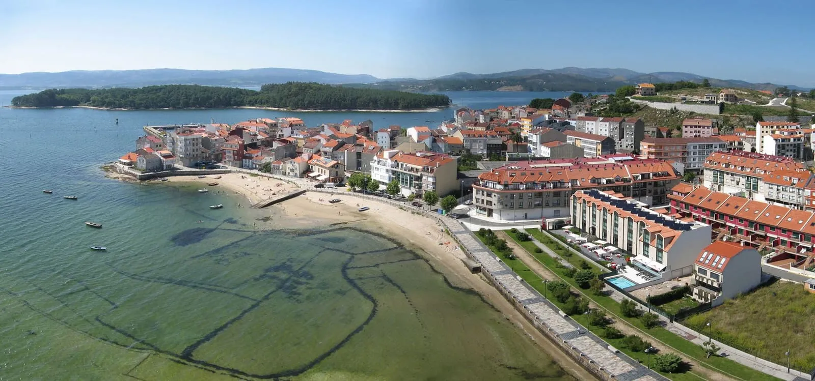 Vista aérea de O Carril, con las casas junto al paseo, la playa y los parques de cultivo de marisco de la ría