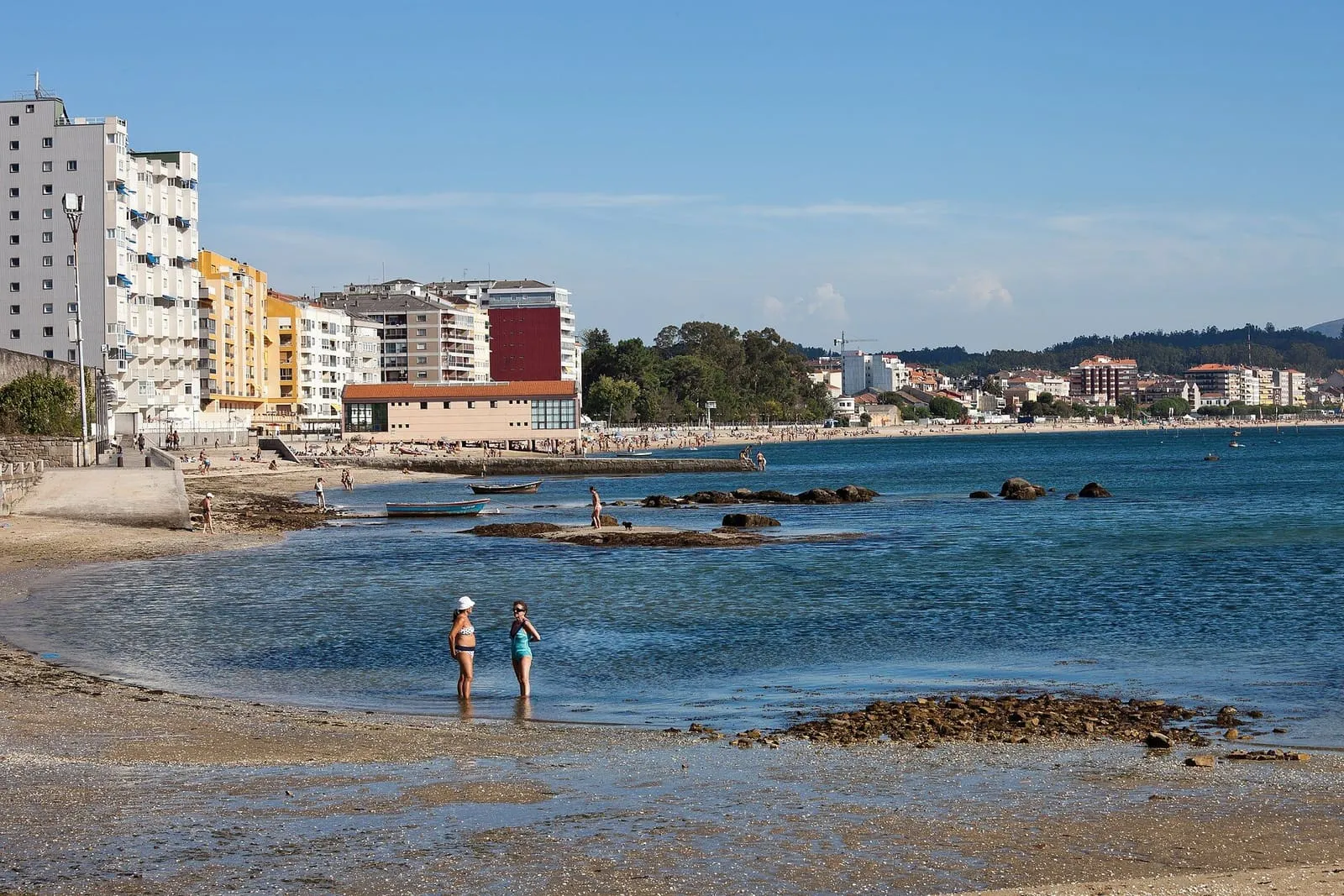 Playa de Compostela con edificios de Vilagarcía al fondo y dos personas en la orilla