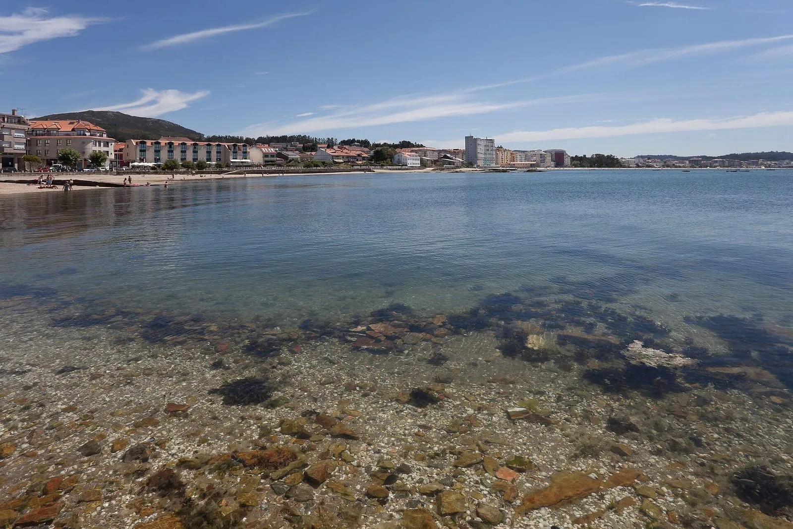 Vista de la ría de Arousa y de Vilagarcía desde la playa de Portugalete, en O Carril, con aguas claras sobre un fondo de rocas