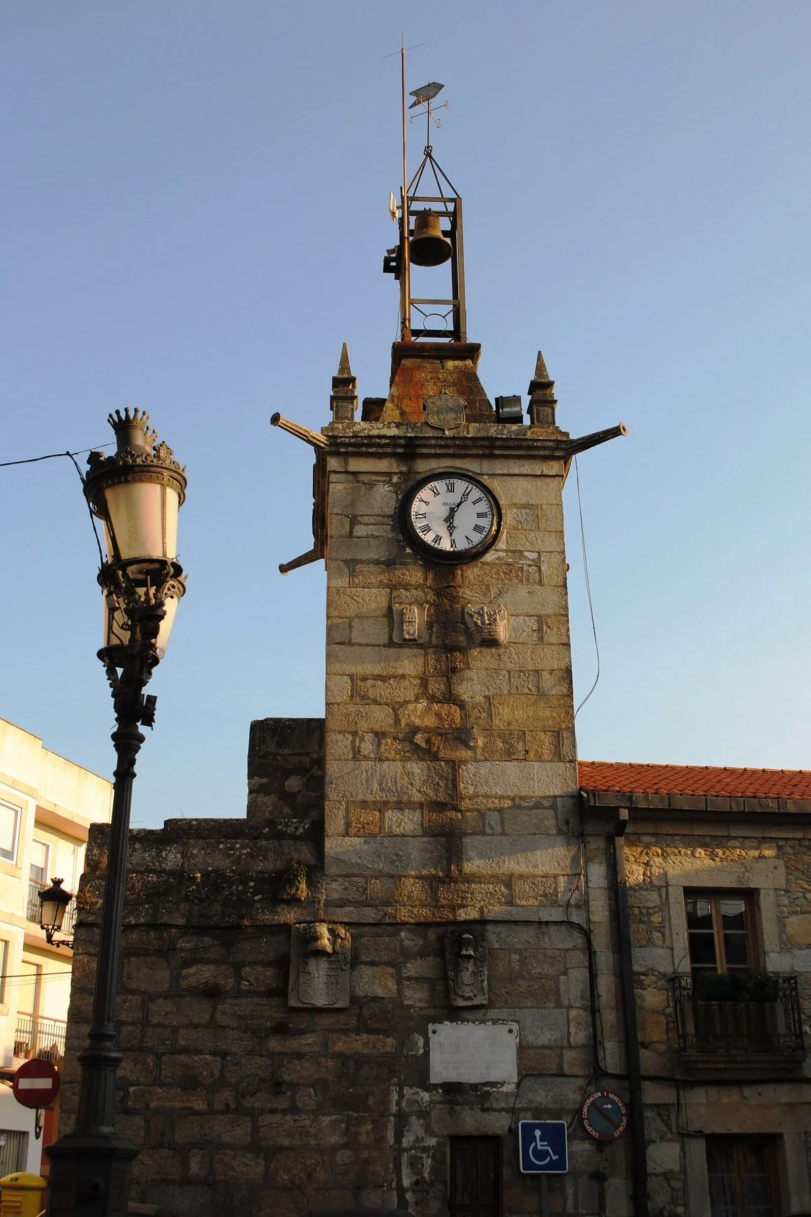 La torre del reloxo de A Guarda, de piedra, con una esfera blanca, junto a una farola