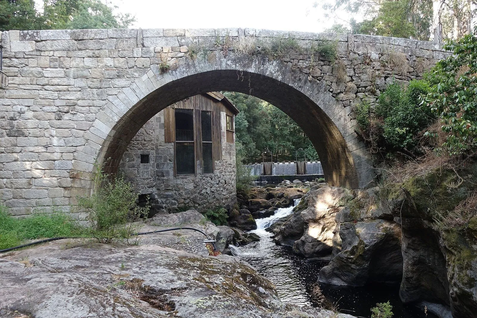El arco apuntado del puente de Mourentán sobre el río Deva, con un molino de piedra al fondo y rápidos debajo
