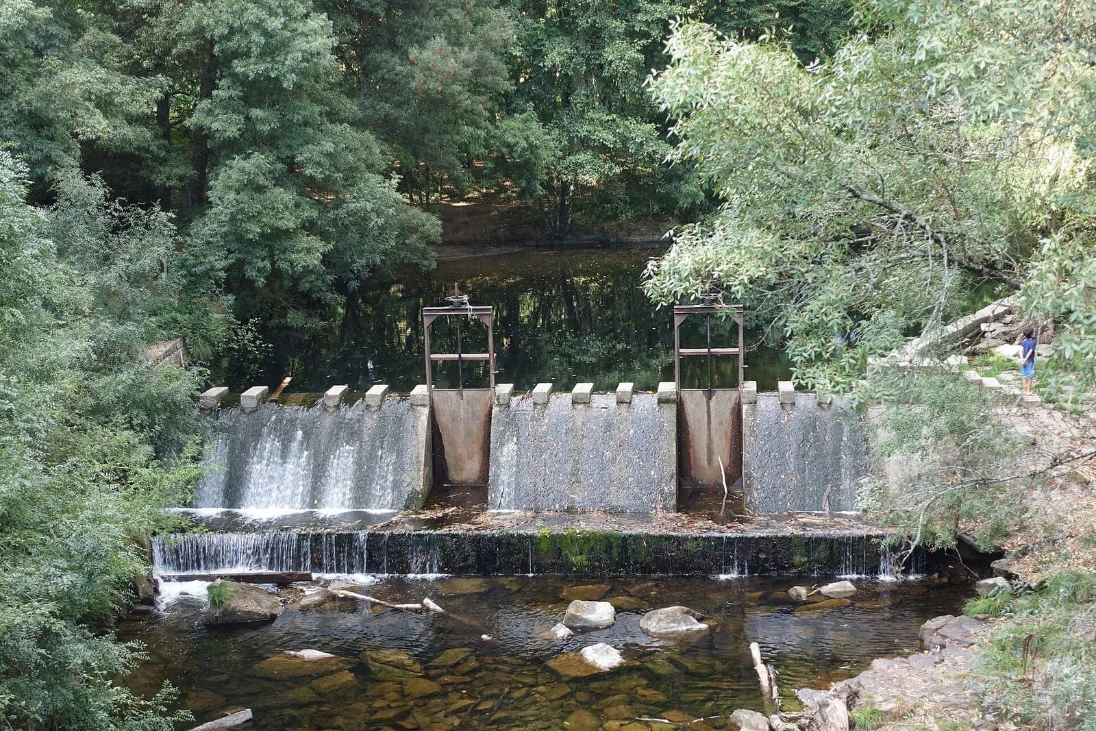 Azud con compuertas y pequeñas cascadas sobre el río Deva, en Arbo, entre árboles