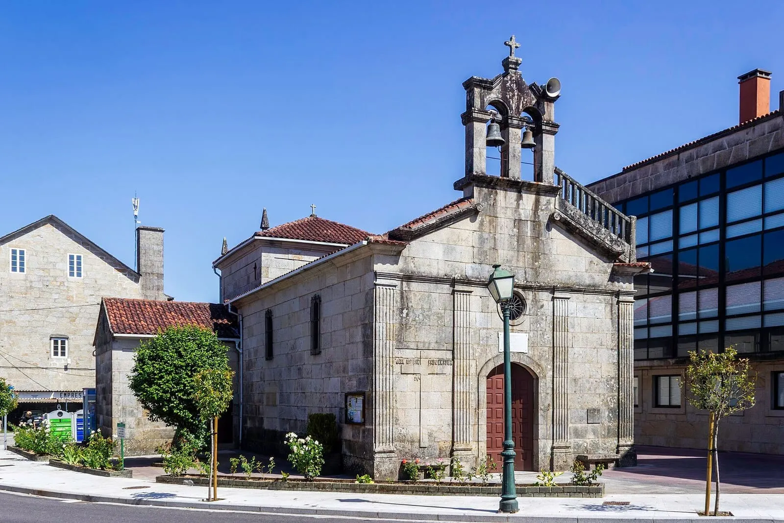 La iglesia de Nuestra Señora de Lourdes, de piedra, con espadaña de tres campanas, junto a un edificio moderno