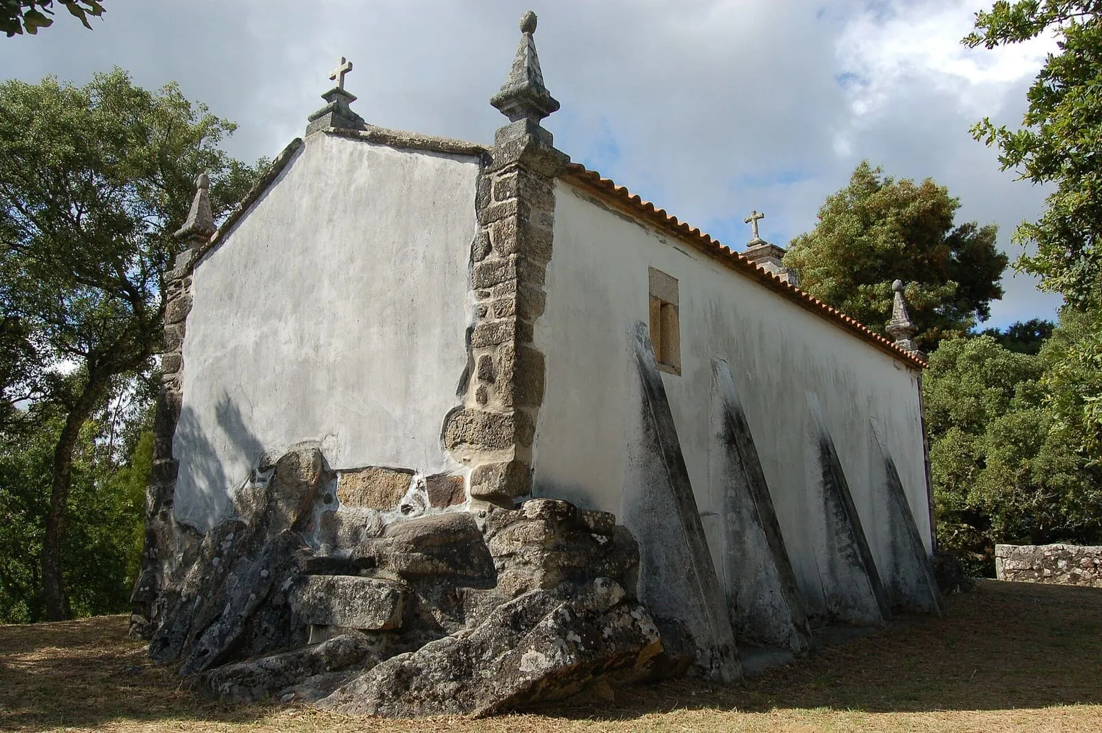 La ermida de Santa María Magdalena, blanca, con grandes contrafuertes de piedra sobre un peñasco en lo alto del monte