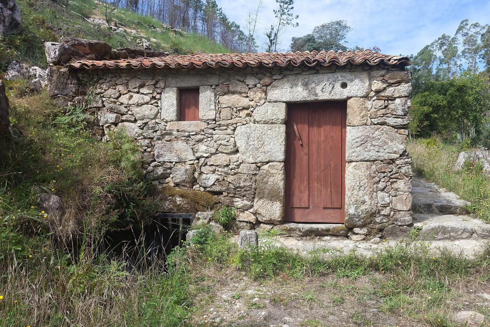 Molino de piedra con tejado de teja y puerta roja en los Muíños do Folón, en O Rosal