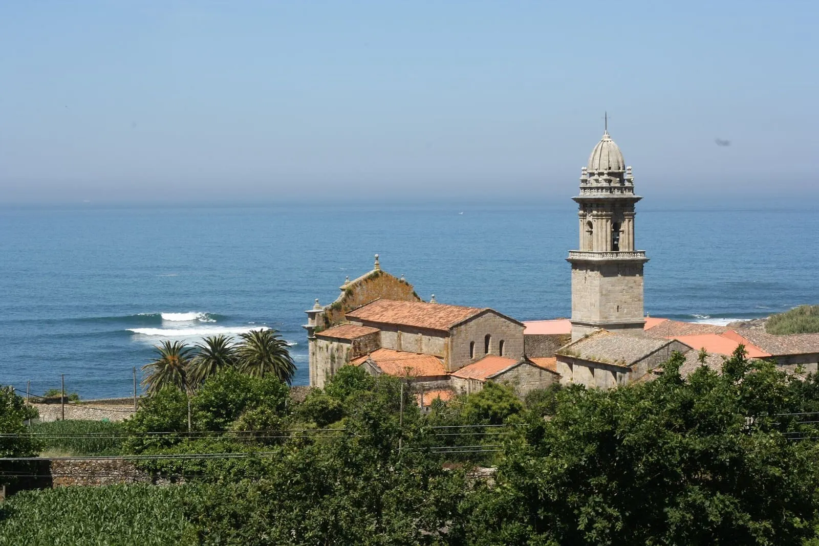 El monasterio de Oia con su torre barroca y el Atlántico con oleaje detrás