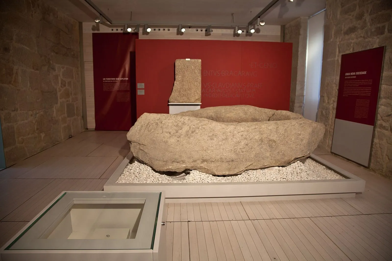 La pía de Mougás, una gran piedra labrada con una cubeta, expuesta sobre un lecho de guijarros en una sala de museo