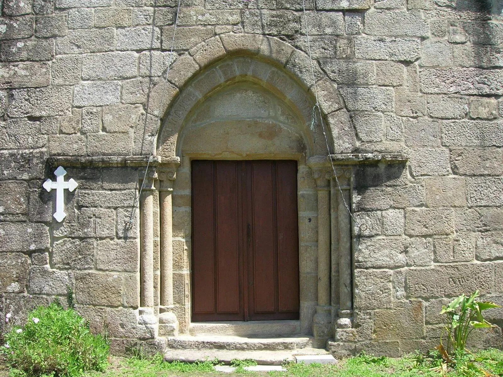 La portada románica de Santo Estevo de Cumiar, con arco de medio punto, columnas y una cruz de piedra