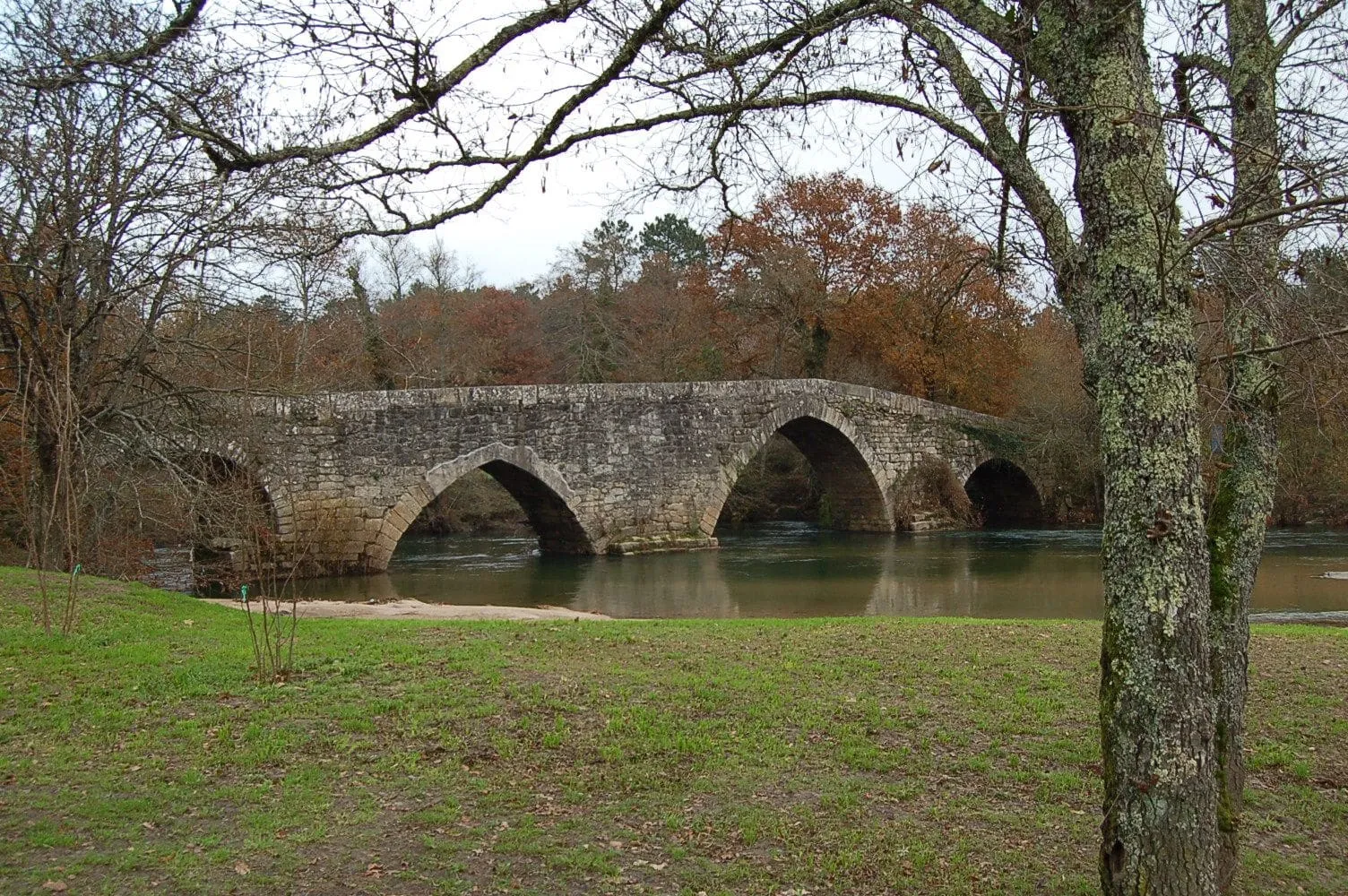 El puente medieval de las Partidas, de varios arcos de medio punto, sobre el río Tea entre árboles de otoño