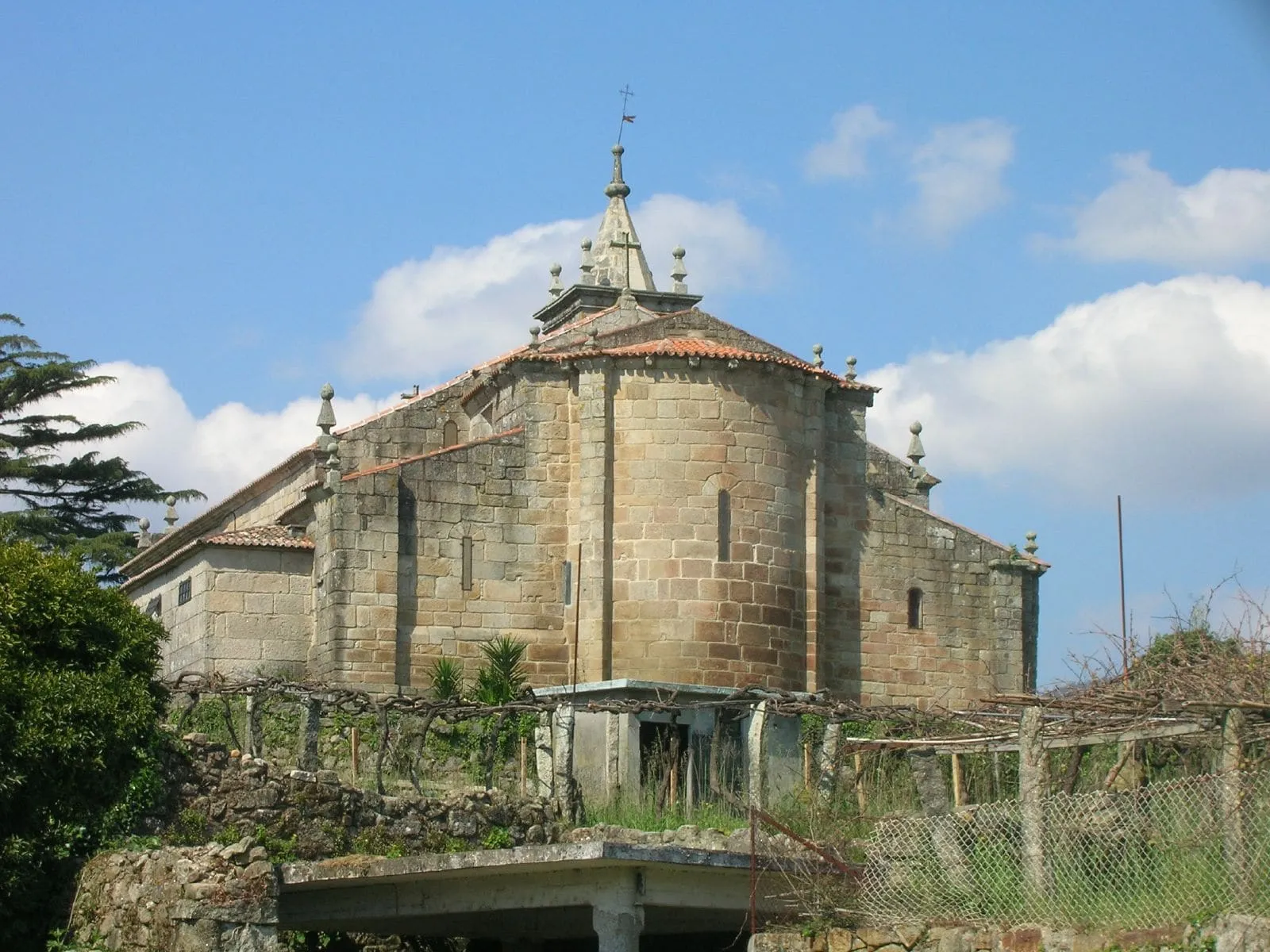 El ábside semicircular de la iglesia de San Bartolomeu de Rebordáns, de sillería dorada, entre viñedos y prados