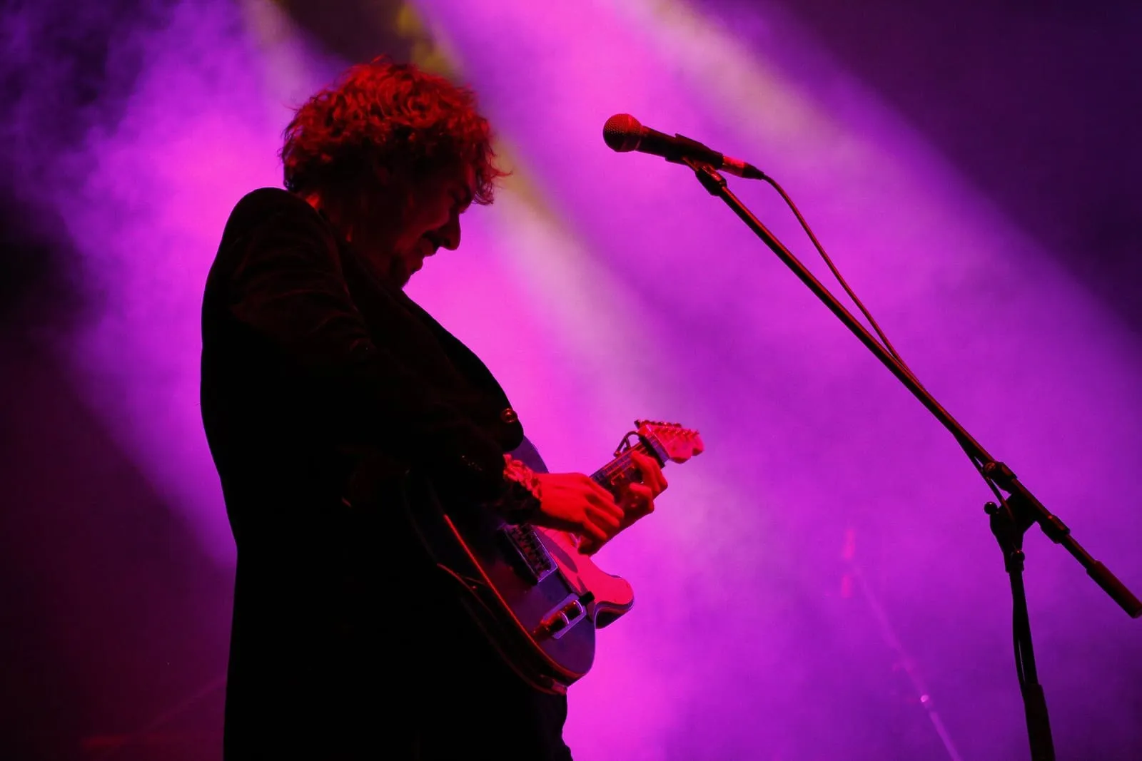Ángel Stanich tocando la guitarra eléctrica a contraluz, bajo focos morados
