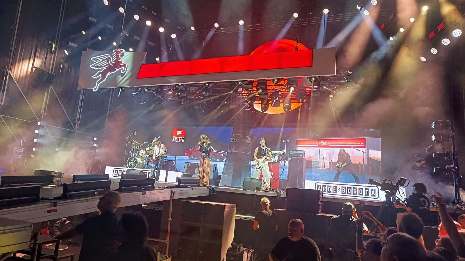 Arde Bogotá tocando en un gran escenario de festival iluminado en rojo, con el público delante