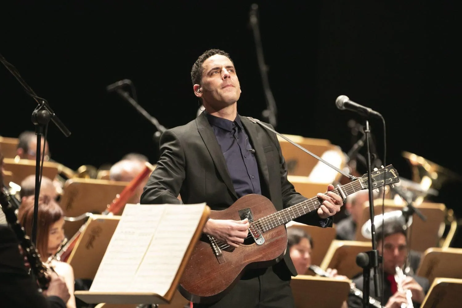 DePedro cantando con guitarra acústica delante de una orquesta