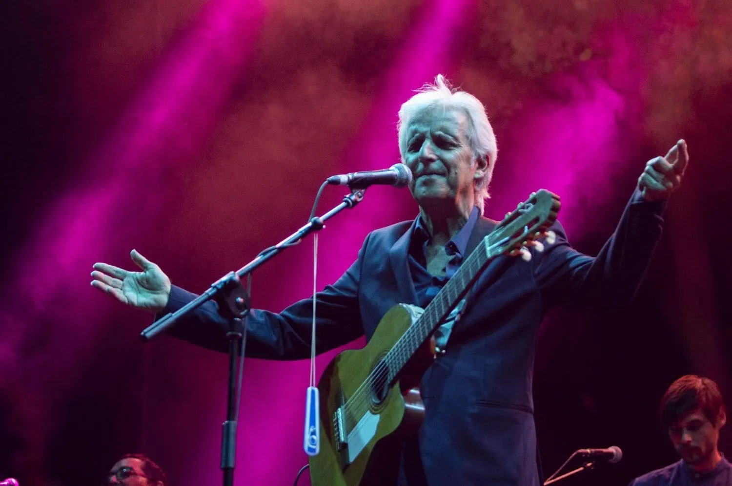 Kiko Veneno canta con los brazos abiertos y la guitarra al hombro en un escenario iluminado de rosa