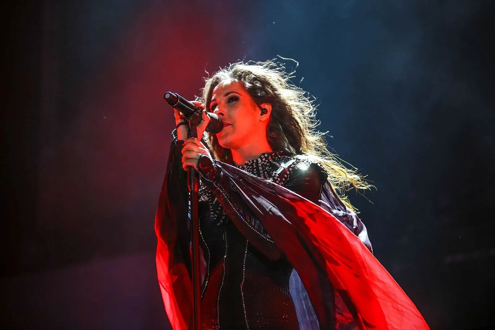 Malú cantando en el escenario con un vestido rojo y negro, bajo focos rojos