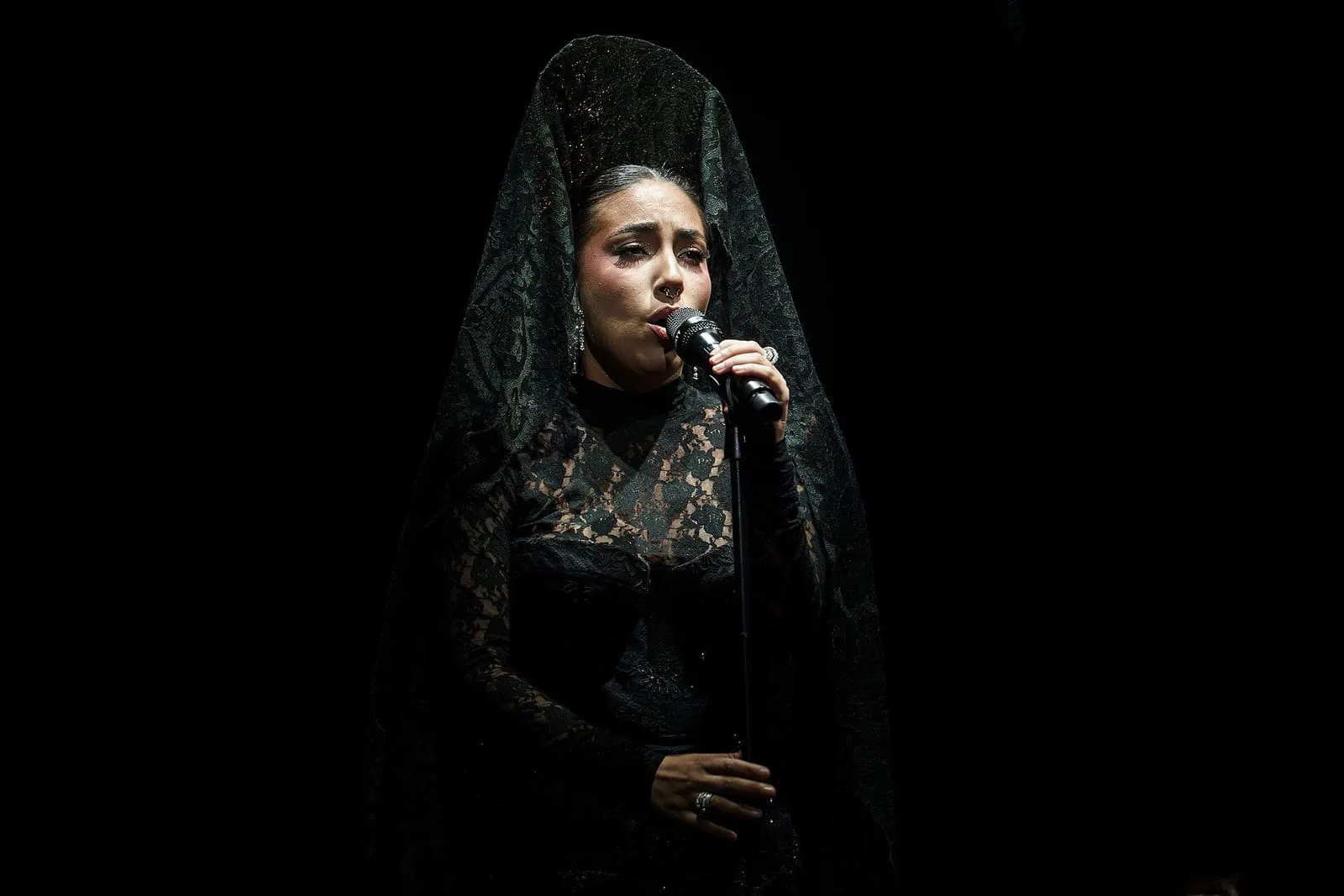 María José Llergo cantando con mantilla negra sobre fondo oscuro
