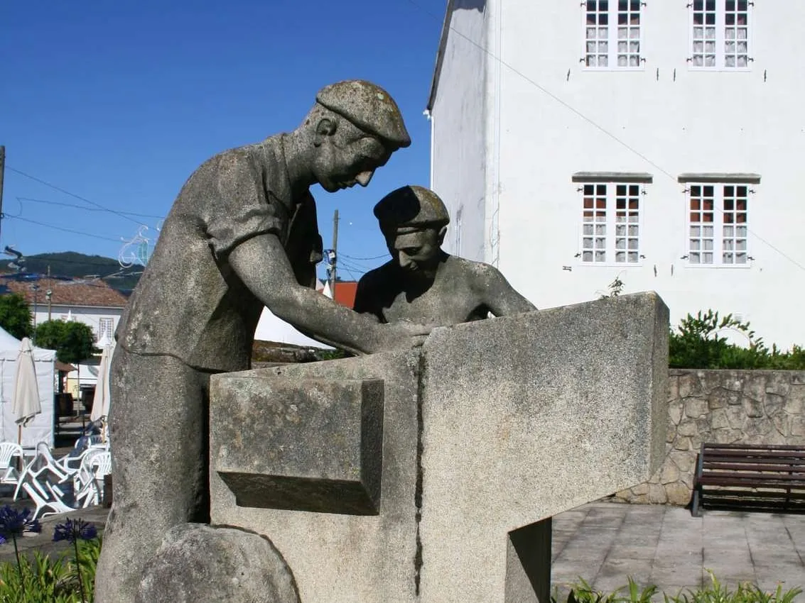 Escultura de piedra de dos cabaqueiros trabajando el barro de las tejas, en O Rosal