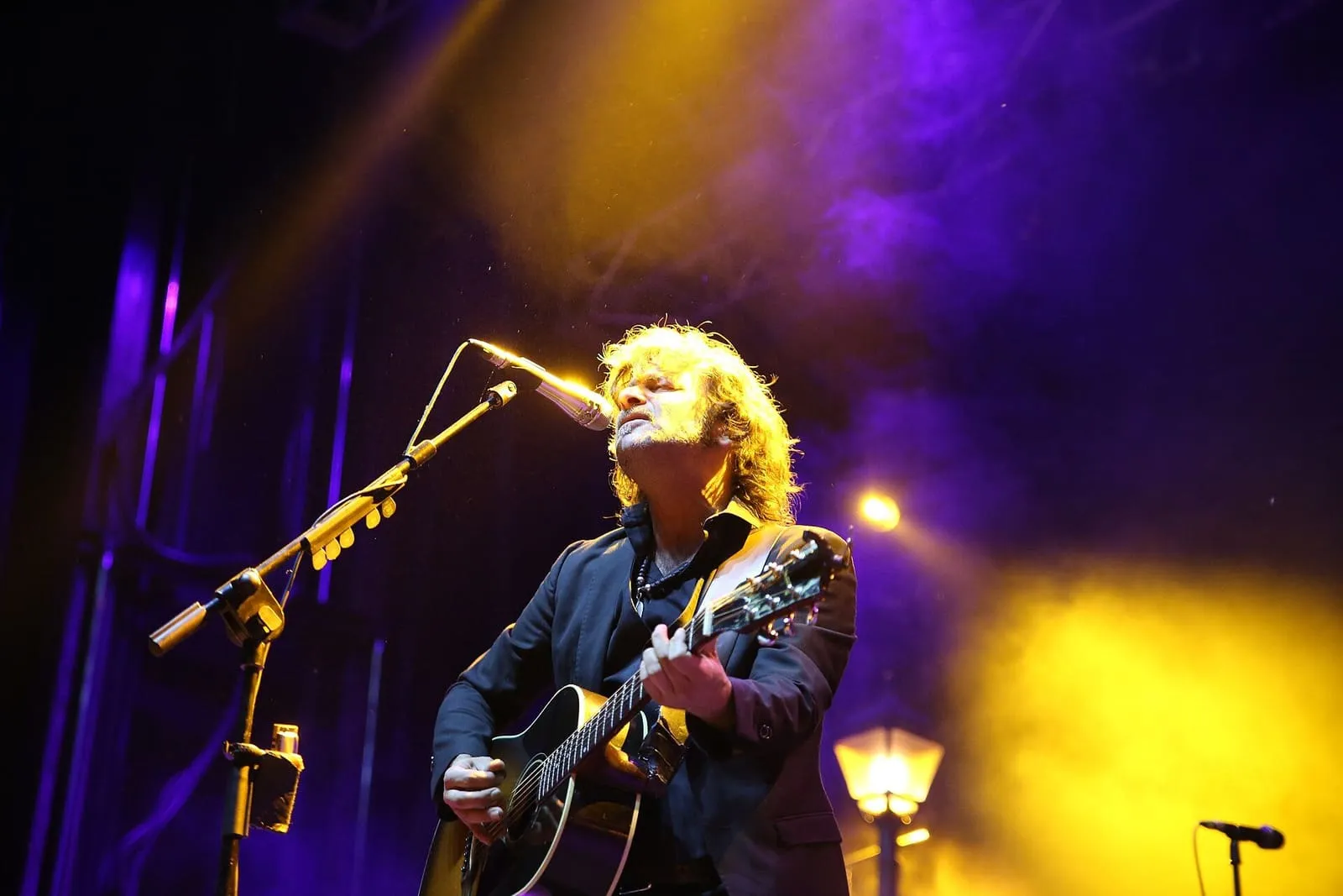Quique González canta con guitarra acústica bajo focos amarillos y morados