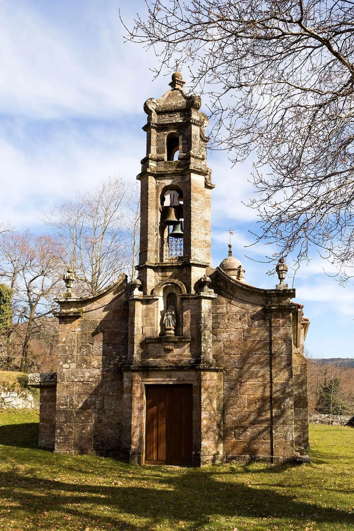 El campanario de piedra de la capela de Gundián, con las campanas a la vista y una hornacina en la fachada