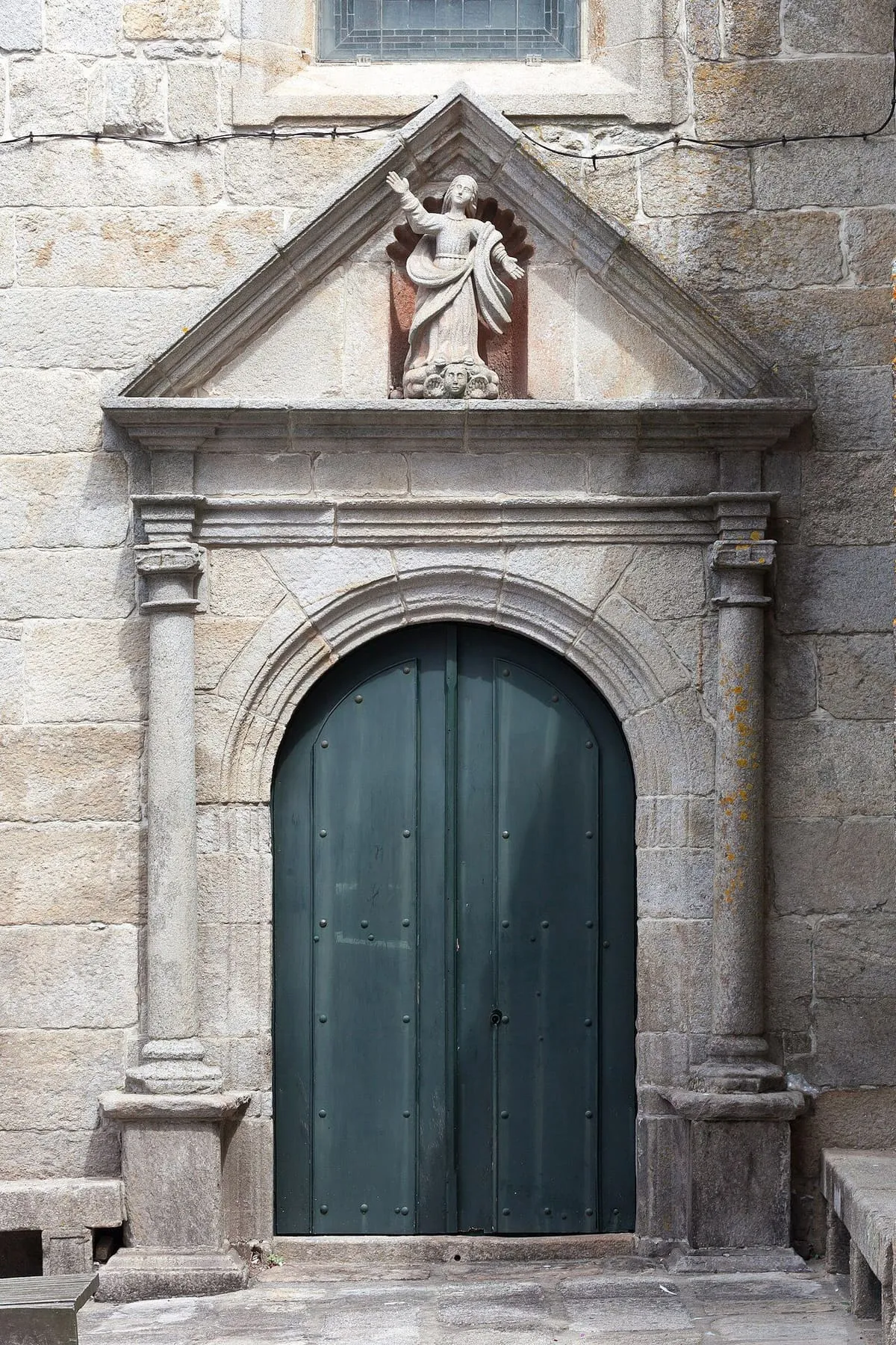 Portada de piedra de la iglesia con arco de medio punto y puerta de madera verde