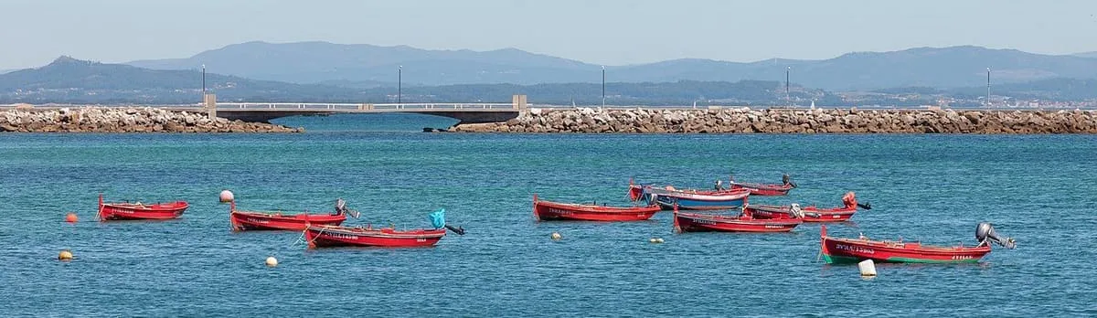 Barcas rojas fondeadas en el puerto de Aguiño con el espigón al fondo