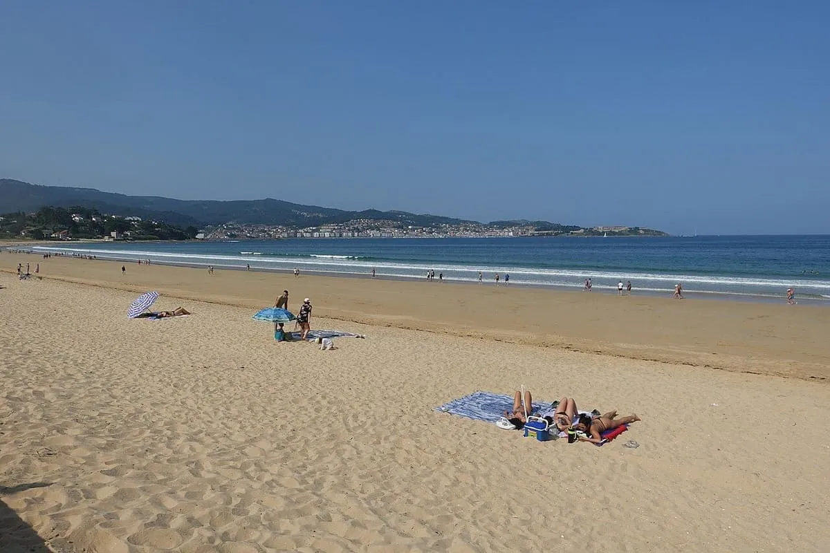 Arena dorada de la playa América con bañistas y el monte al fondo