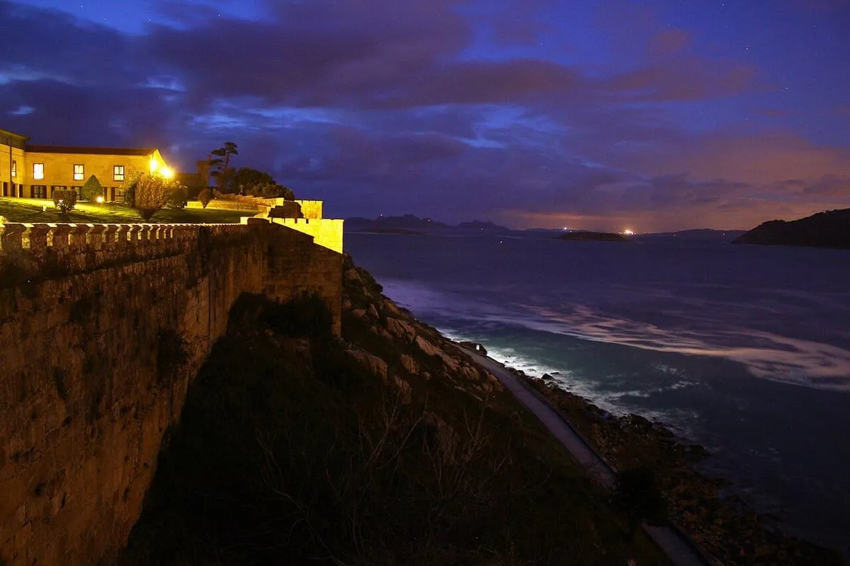 Muralla y Parador de Monterreal iluminados al anochecer sobre el Atlántico