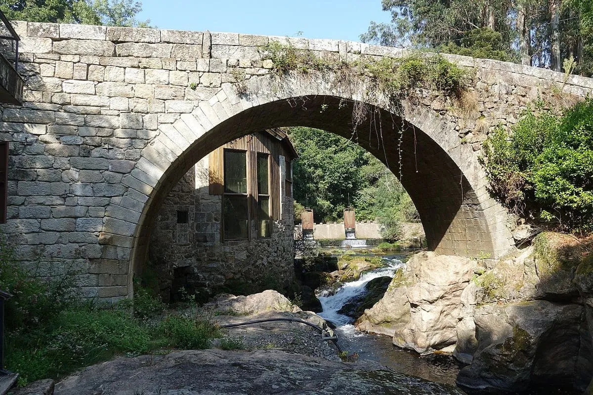 El puente visto desde el cauce, con el arco, un molino de madera y piedra y las rocas del río