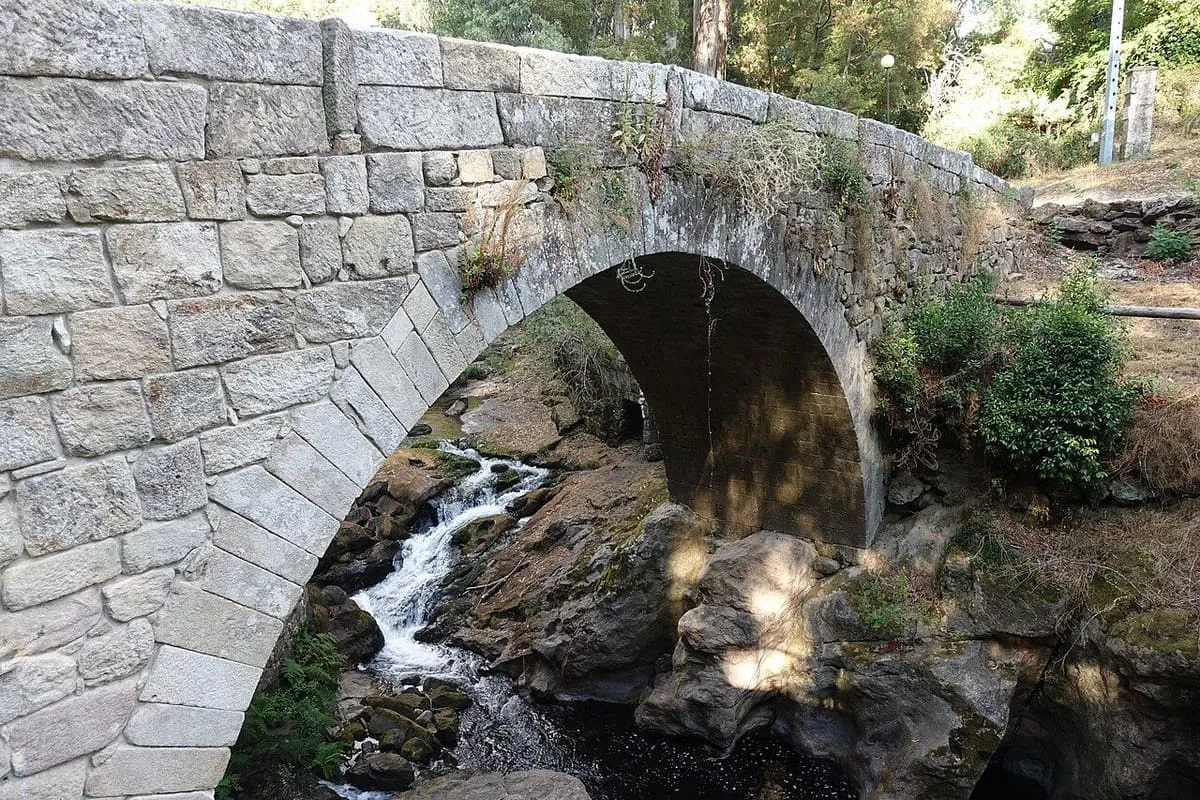 El arco del puente de piedra y los pequeños rápidos del río Deva entre rocas