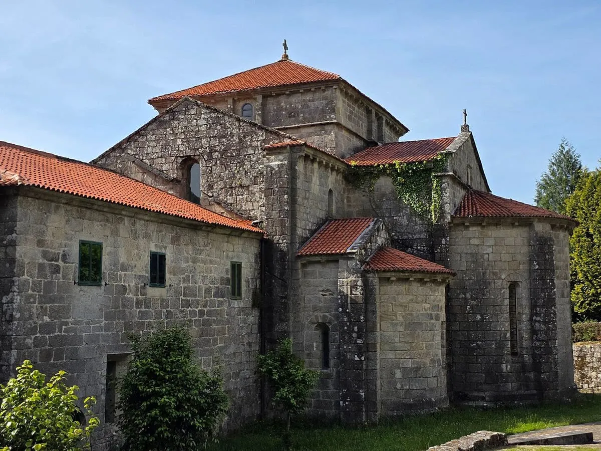 Ábsides de la iglesia de Armenteira con tejados de teja bajo un cielo azul