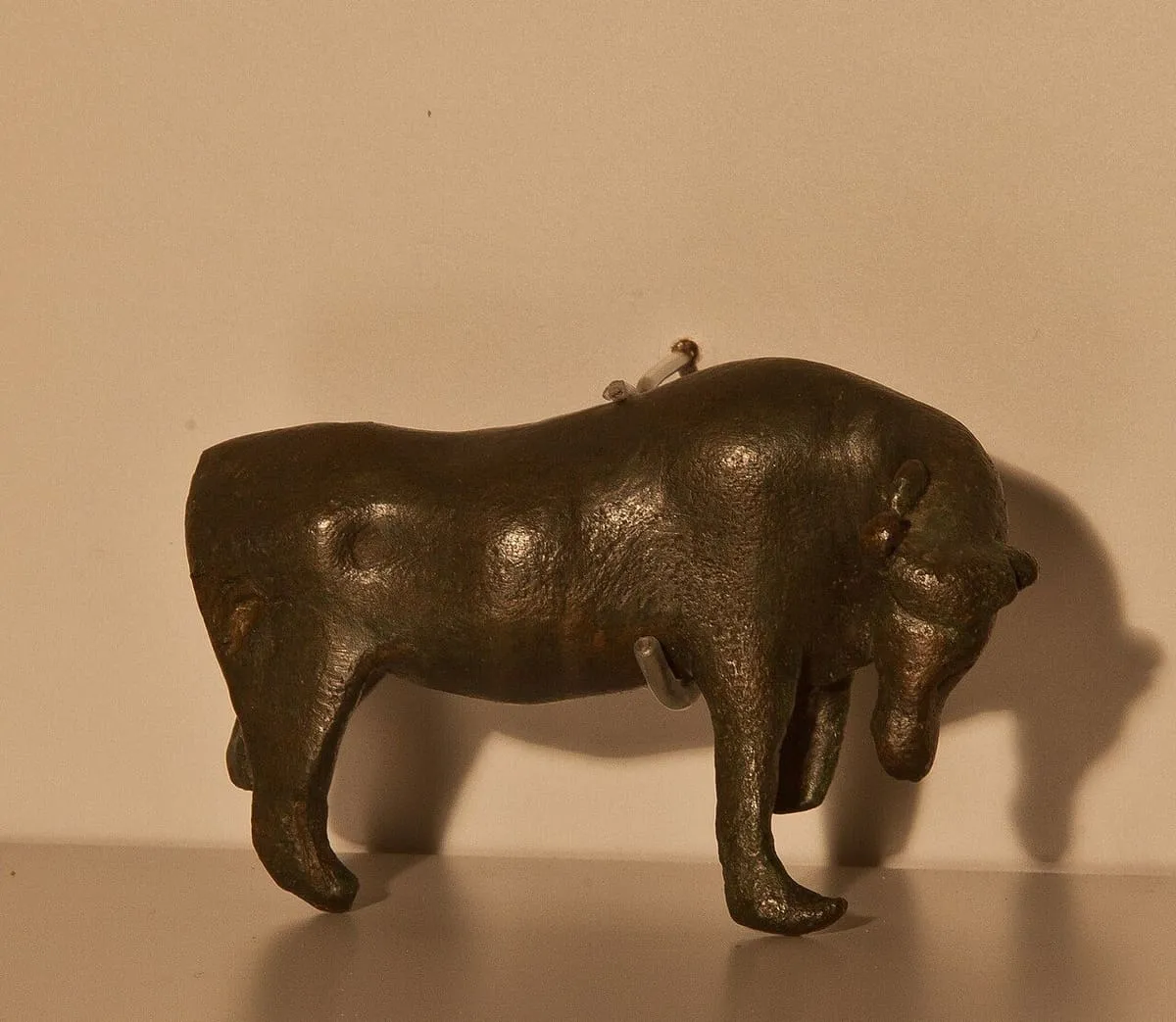 Figura de bronce de un bóvido, de perfil, sobre una peana blanca