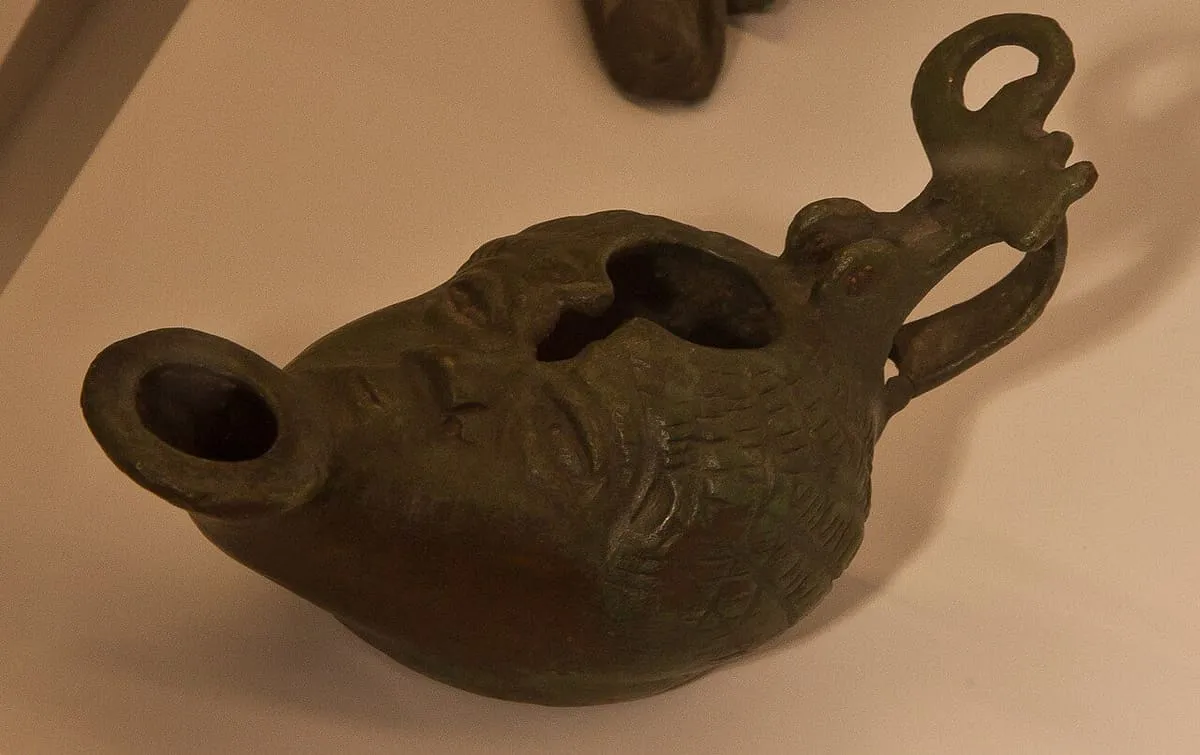Lucerna de bronce con forma de rostro, con el pico para la mecha y un asa