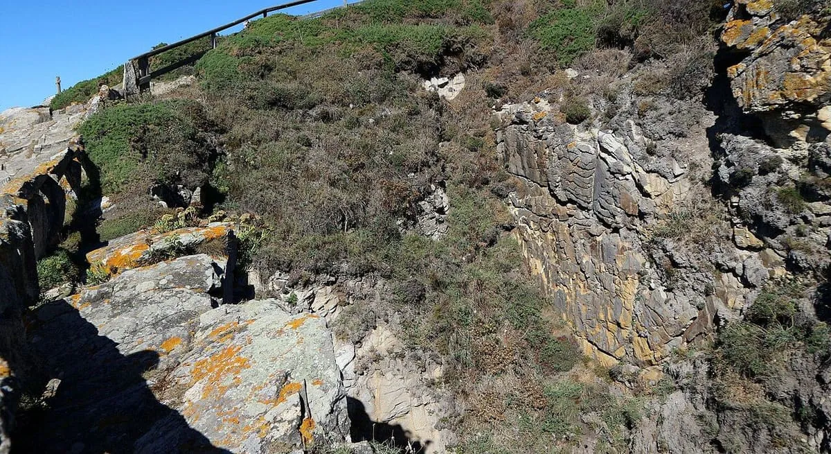 El cantil de roca oscura y liquen anaranjado sobre el Buraco do Inferno