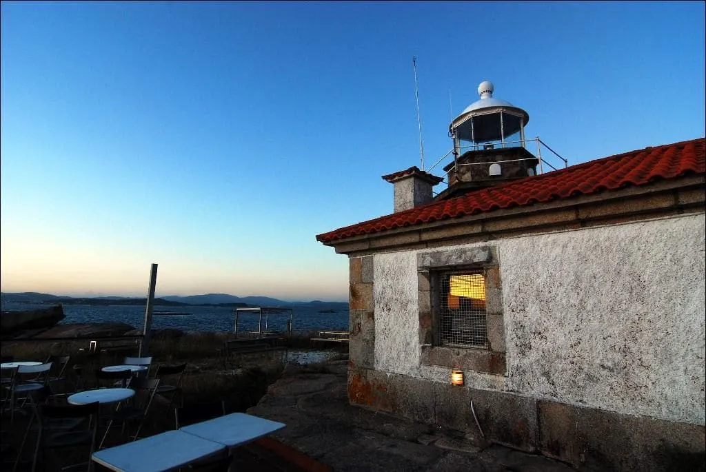 Linterna y edificio blanco del faro con una terraza con mesas frente al mar