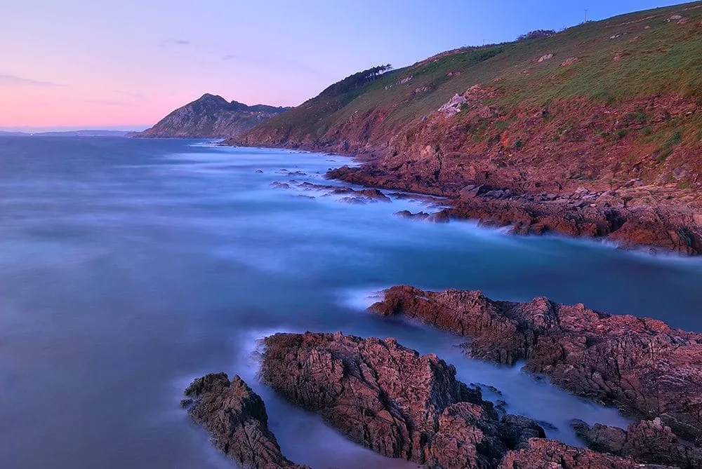 Costa rocosa de Cabo Home al atardecer, con acantilados rojizos y el mar suave