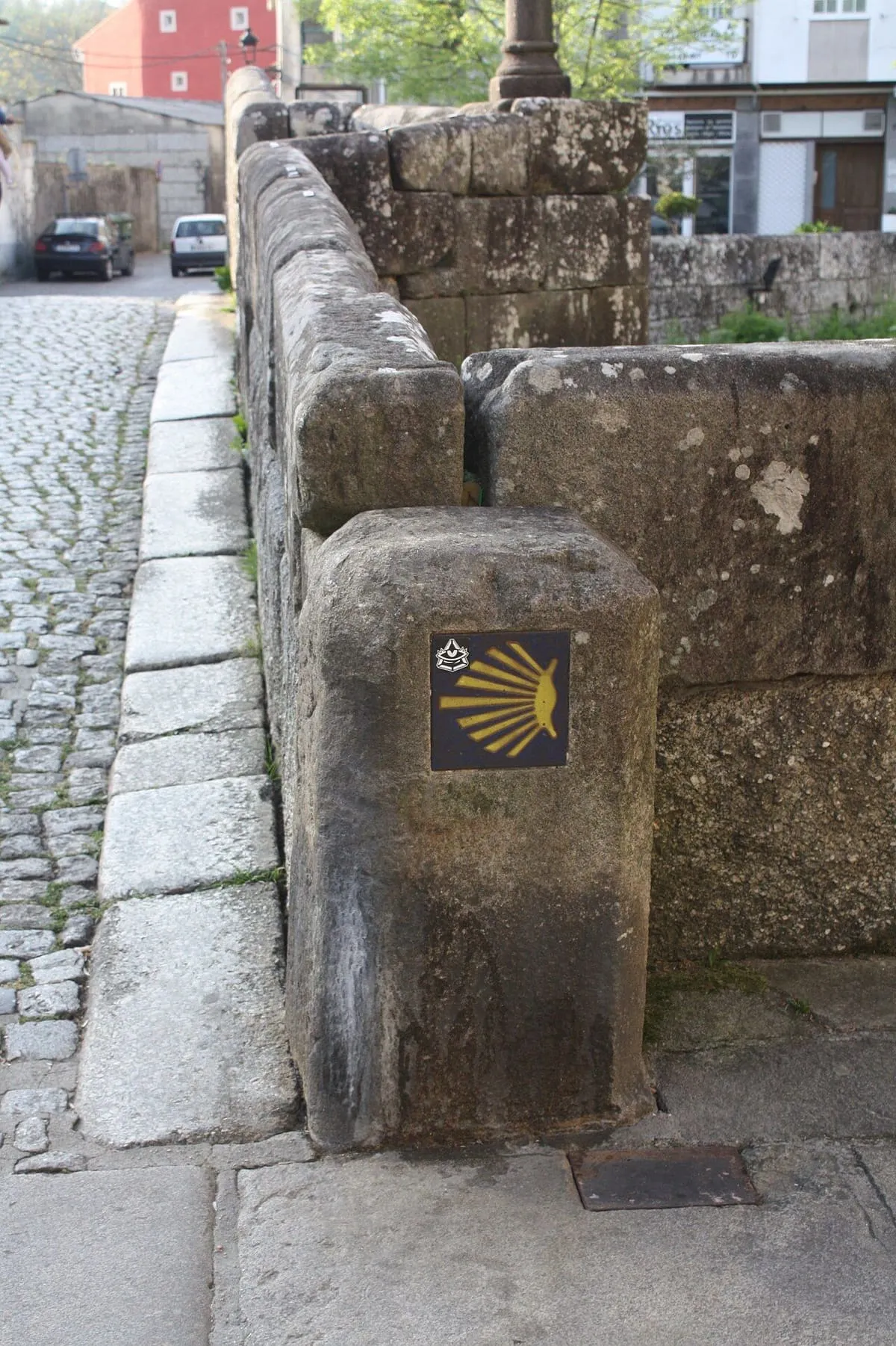 Un mojón de piedra con la concha del Camino de Santiago junto a la ponte da Bermaña