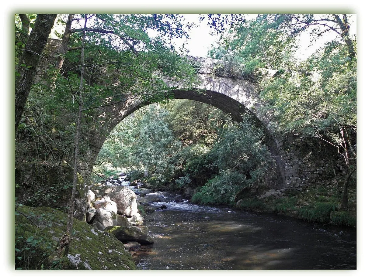 Puente de piedra sobre un río entre árboles, en el entorno de Caldas de Reis