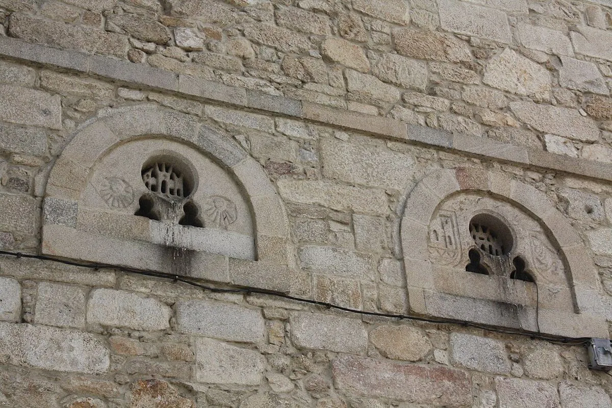 Dos arcos de medio punto con ventanas de piedra calada y relieves, en el muro lateral de la iglesia
