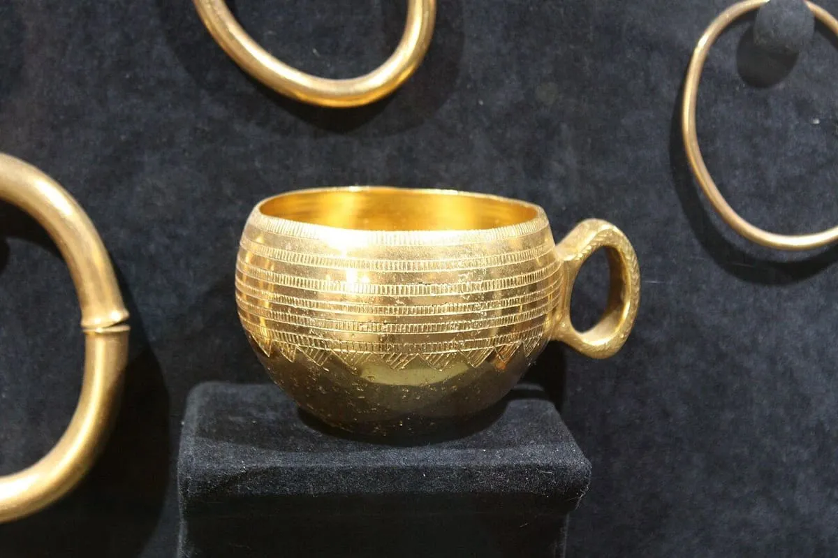 Una taza de oro con una sola asa y finas líneas grabadas, entre aros dorados