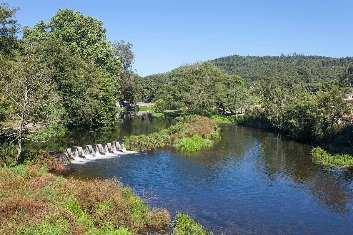 El río Umia con una pequeña presa y arbolado a su paso por Caldas de Reis