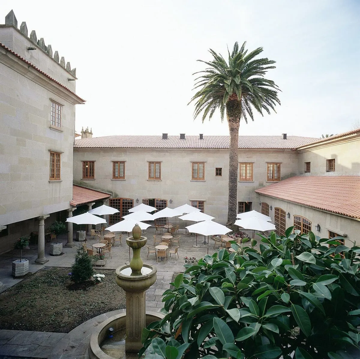 Patio con soportales y fuente del parador de Cambados, con una palmera y mesas con sombrillas