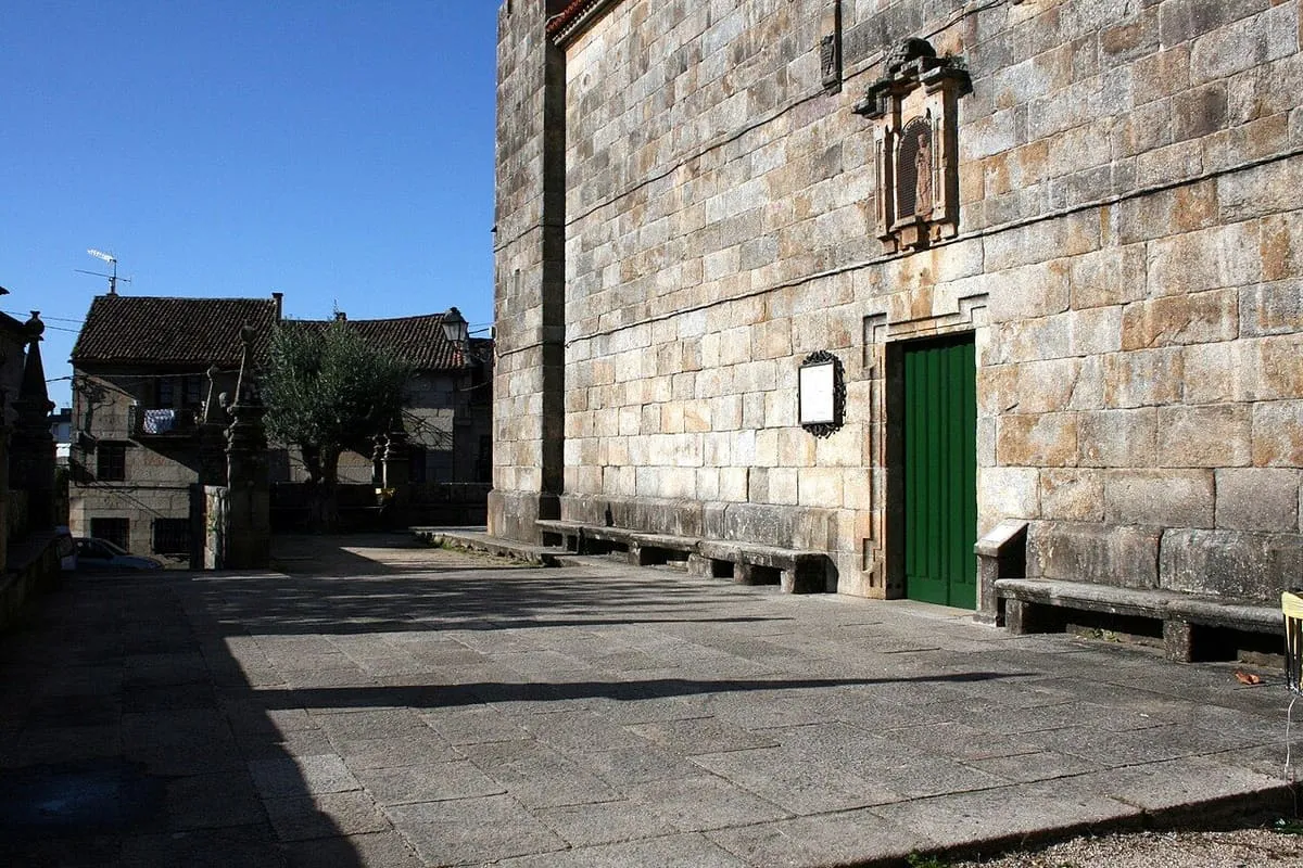 Atrio lateral de la iglesia de San Benito, con bancos de piedra y una puerta verde