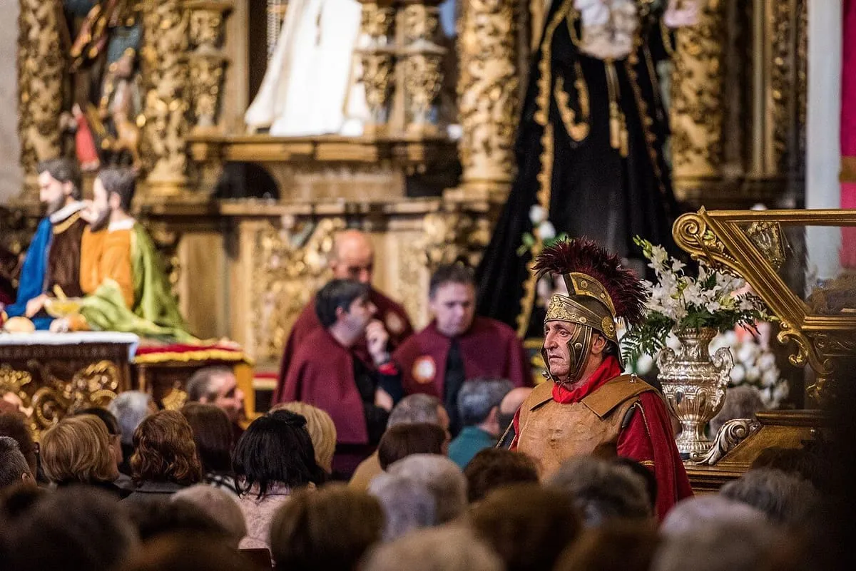 Un centurión romano con armadura roja junto a niños y fieles durante la ceremonia