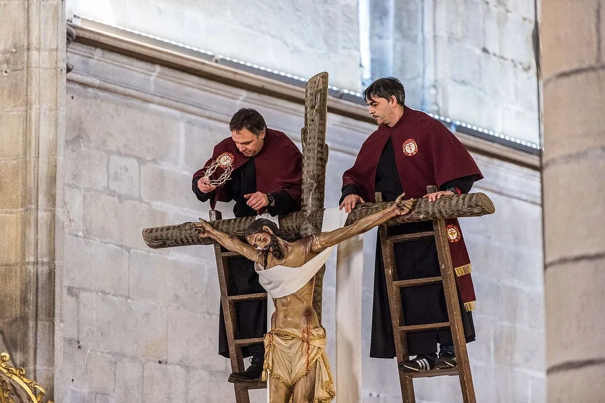 Cofrades con túnicas granates descendiendo la imagen de Cristo de la cruz con la ayuda de una escalera